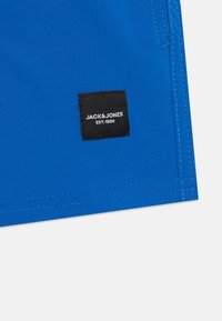 Blå tygshorts med platt sömnad. Svart vävd etikett med "JACK&JONES" och "EST. 1990" i vit text nere i hörnet.