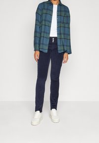 Rutig skjorta i blått och grönt, avslappnad passform med knappar; ihop med marinblå kordbyxor med treknappsfront och vita träningsskor.