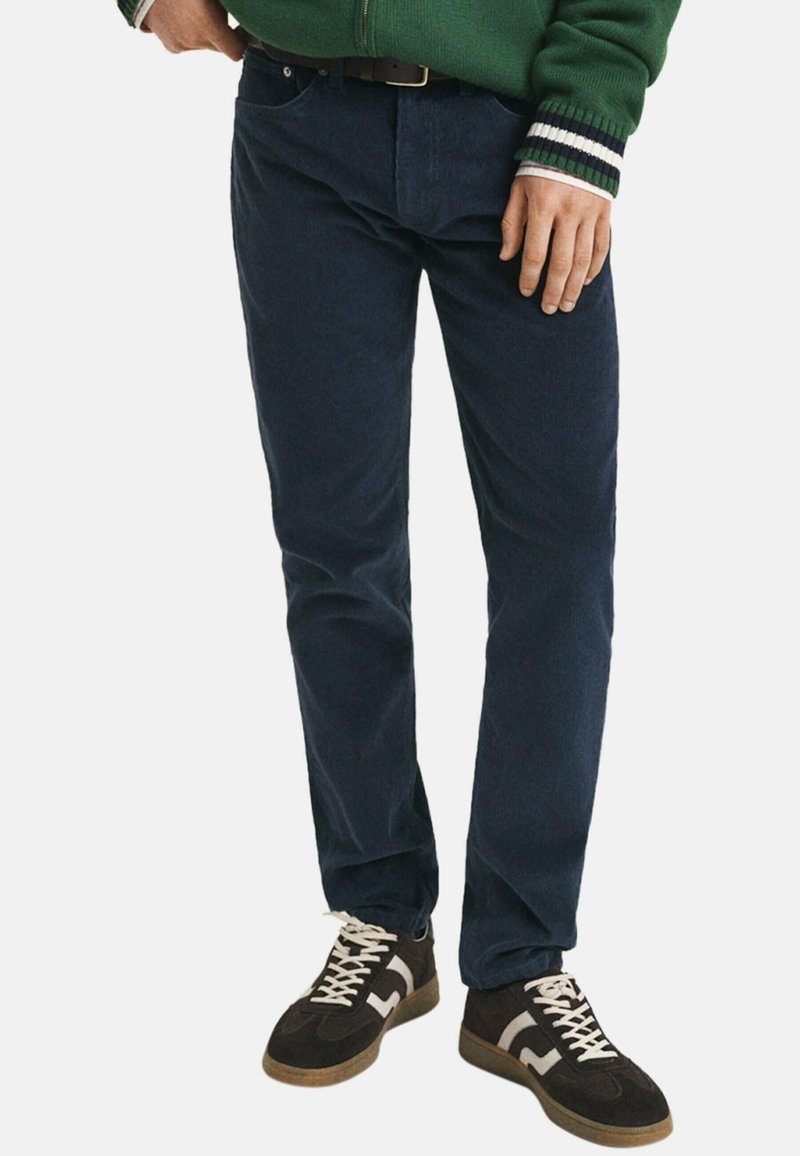 Marineblauwe corduroy broek met een rechte pasvorm, voorzien van een klassieke vijfzakkenontwerp, en gecombineerd met donkere sneakers en een groen zip-up jack.