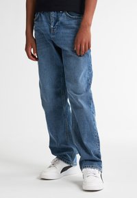 Jeans in denim azzurro chiaro con vestibilità comoda, dotati di cinque tasche, chiusura con bottone e dettagli di cucitura. Indossati con sneakers bianche.