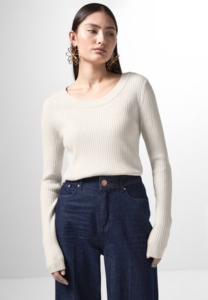 Geribbelde gebreide trui in beige met een brede halslijn, gecombineerd met donkerblauwe wijde broekspijpen. Opvallende lange mouwen en een aansluitende structuur.