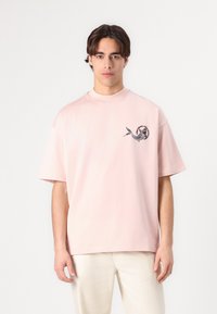 Pink cotton t-shirt with short sleeves and a high neckline, featuring a circular graphic design with a serpent in blue and black on the chest.