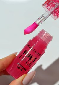 Olio per labbra idratante in un tubetto trasparente rosa. Presenta un applicatore morbido con tonalità rosa, etichettato "REVIEW POUT LIP OIL."