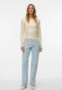 Helekreemikas pikkade varrukatega nööbitav pluus, sobitatud tuhmunud siniste laia säärega teksadega, millel on pitsist lillemustriga pealmine kiht. Neutraalset tooni plokkkontsaga kingad.