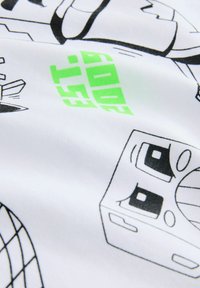 Bílá látka s černými ilustracemi v kresleném stylu a zeleným textem. Design obsahuje různé hravé tvary a tváře, s hladkým povrchem.