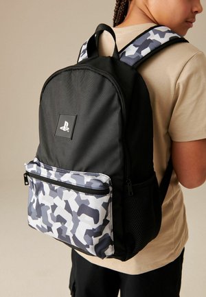 Person wearing black backpack with white and gray patterned front pocket and shoulder straps, featuring a PlayStation logo.