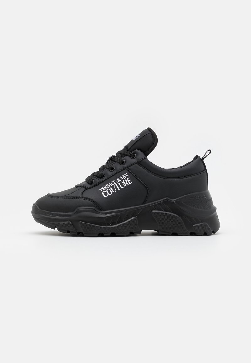 Black athletic sneakers featuring a smooth synthetic upper, chunky rubber sole, lace-up design, and logo detail on the side.