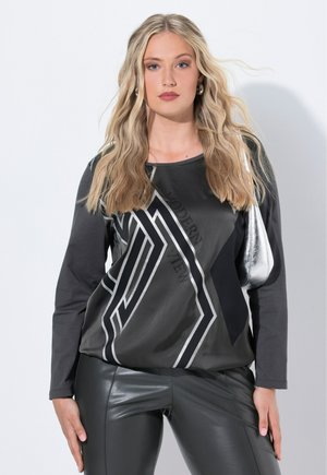 Langsleeve top met een zwart en grijs geometrisch ontwerp, voorzien van metallic accenten en een gladde textuur, gecombineerd met glanzende zwarte leggings.