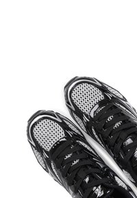 Chaussures de sport noir et blanc avec une tige en maille, des accents brillants, des lacets texturés et une semelle contournée.