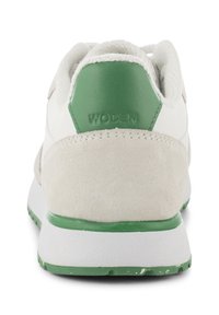 Baskets blanches avec des accents verts, dotées d'un talon en daim texturé et d'une semelle en caoutchouc lisse. "WODEN" est embossé sur le talon.