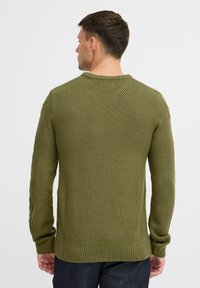 Pulover tricotat de culoare verde măslin, cu un model texturat, guler rotund și manșete și tiv cu cotiță. Purtați pe dos, afișând designul din spate.
