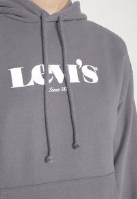 Sudadera gris con capucha ajustable y bolsillo frontal. Presenta el logo blanco "LEVI's" y el texto "Desde 1873". Textura suave, diseño casual.