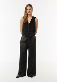 Black suede vest with a deep V-neck and front buttons, paired with wide-leg black leather pants and pointed toe black heels.
