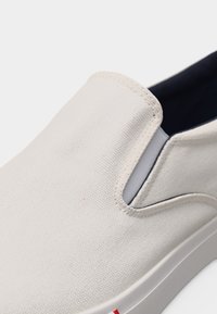 Κοντινό πλάνο λευκού κανβά παπουτσιού χωρίς κορδόνια με ελαστική πλαϊνή επένδυση και λευκή λαστιχένια σόλα.