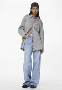 Oversized gray denim shirt with a front pocket, paired with light blue wide-leg jeans. Black shoes complete the outfit.