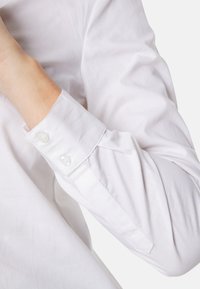 Camicia bianca a maniche lunghe con polsini abbottonati, realizzata in tessuto di cotone morbido e con un design a colletto classico. Linee pulite e dettagli minimali.