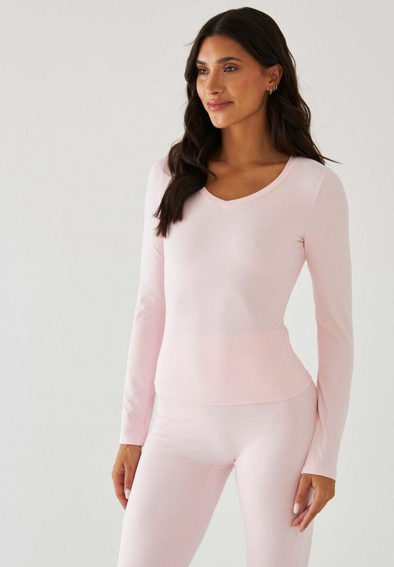 Bluzka z długim rękawem i dekoltem w serek, jasnoróżowa, o gładkiej fakturze. Dopasowana sylwetka, zestawiona z dopasowanymi jasnoróżowymi legginsami. Minimalistyczny design.