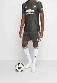 Musta ja harmaa Manchester United -jalkapallopaita, jossa on aaltoaskelkuvio, Chevrolet-logo, yhdistettynä vihreisiin shortseihin, valkoisiin sukkiin ja jalkapalloon.