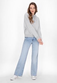 Hanorac gri deschis cu glugă ajustabilă, asortat cu blugi largi de un albastru deschis. Materialele par moi, având un design casual și confortabil.