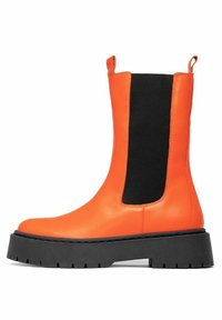 Oranžová kožená kotníková bota s černým elastickým bočním panelem a silnou černou gumovou podrážkou. Má kulatou špičku a poutko pro snadné obutí.