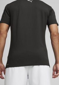 Černé sportovní tričko vyrobené z hladké tkaniny, s kulatým výstřihem, krátkými rukávy a malým bílým logem na zadní straně blízko výstřihu.