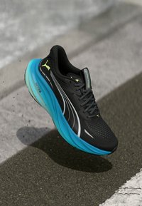 Black athletic shoe with a textured upper, grey accents, and a cushioned turquoise sole. Features reflective stripes and a logo.