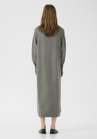 Dlouhé šedé pletené šaty s volným střihem, spadlými rameny a rovnou siluetou. Obsahují rozparek na zadní straně a jednoduchý, minimalistický design.