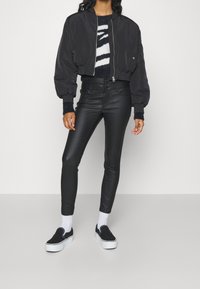 Svart kort bomberjacka med puffärmar, kombinerad med högmidjade svarta skinny jeans och svarta slip-on sneakers. Vita ankelsockor synliga.