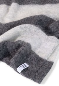 Pezzo morbido di coperta in misto lana con strisce orizzontali grigie e bianche, caratterizzato da una superficie testurizzata e un piccolo etichetta bianca sul bordo.
