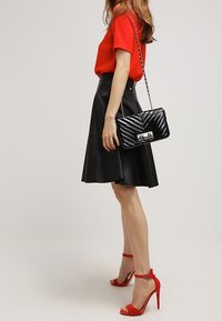 Svart konstläderskjol, röd kortärmad topp och röda klackskor med ankelsnörning. Svart vadderad handväska med silverdetaljer och kedjestropp.