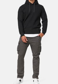 Zwarte hoodie met trekkoorden, gecombineerd met grijze cargobroeken met zijzakken. Witte sneakers met zwarte accenten maken de look compleet.