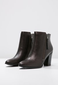 Stivaletti alla caviglia in finta pelle nera con un motivo a serpente testurizzato, dotati di cerniere laterali e un tacco alto affusolato. Design a punta.