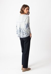 Gray sweater with blue landscape print, long sleeves, and a pleat detail at the back, paired with tailored black trousers and beige shoes.