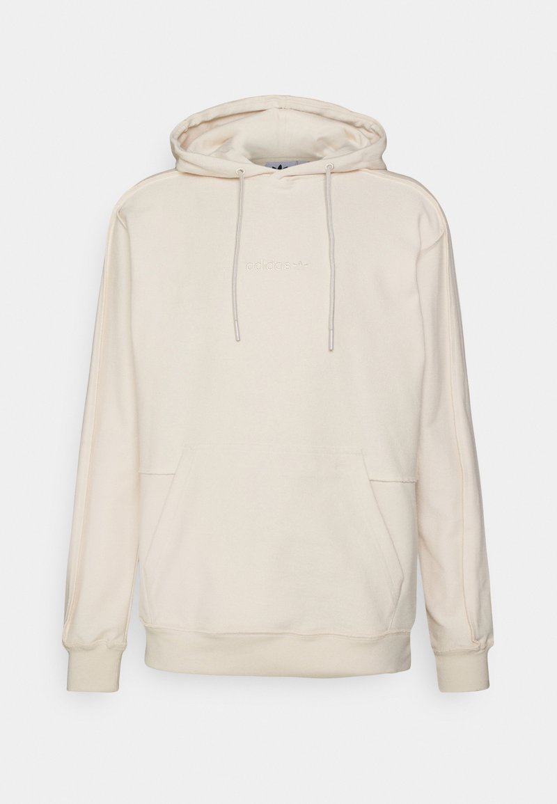 Beige huppari, jossa on kiristettävä huppu, kengurulompakko ja brodeerattu logo rinnassa. Pehmeä kangas, jossa on ribbaus hihansuissa ja helman kohdalla.