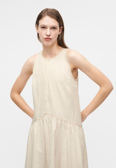 Φωτεινό μπεζ αμάνικο φόρεμα με στρογγυλή λαιμόκοψη, κλείσιμο με φερμουάρ και φούστα με πιέτες. Μαλακό ύφασμα με ορατές ραφές.