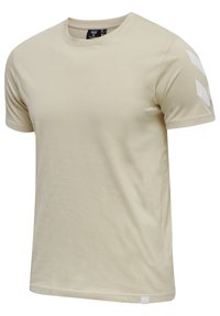 Lys beige kortærmet t-shirt med rund hals, lavet af blødt stof, har hvide, vinkelformede detaljer på venstre skulder og et lille mærke i kanten.