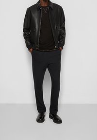 Läderbomberjacka i svart, bärs över en svart skjorta. Löst sittande mörka byxor och svarta ankelskor. Minimalistisk övergripande look.