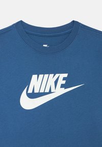 Niebieski bawełniany t-shirt z okrągłym dekoltem, z dużym białym logo Nike i symbolem Swoosh na przodzie. Gładka tekstura, standardowy krój.