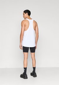 Λευκό αμάνικο τοπ, μαύρο σορτς συμπίεσης, μαύρα αθλητικά παπούτσια και μαύρες κάλτσες. Ομαλό ύφασμα, εφαρμοστή γραμμή, ελάχιστες λεπτομέρειες.