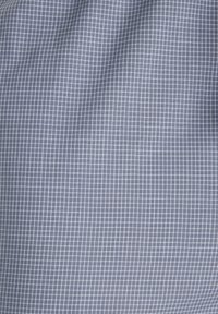 Modrá tkanina s malým bielym kockovaným vzorom, mierne pokrčená, vytvárajúca jemné variácie svetla a tieňa.