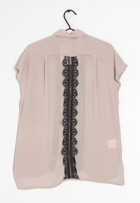 Light beige blouse with short sleeves, a collar, and a central black lace panel. The fabric is sheer with a subtle texture and a relaxed fit.