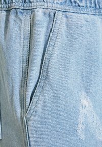 Shorts de denim azul claro con una ligera textura desgastada, bolsillos laterales y un detalle deshilachado en el frente. Cintura elástica para mayor comodidad.