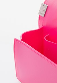 Rosa synthetische Handtasche mit glatter Textur, gebogenen oberen Kanten und einem silbernen Verschluss. Das Innere verfügt über zwei getrennte Fächer.