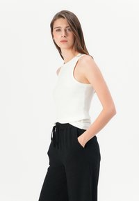 Witte geribbelde tanktop met hoge halslijn, gecombineerd met losse zwarte joggerpants, voorzien van zijzakken en een tailleband met trekkoord.