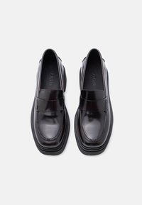 Mocassins en cuir noir avec une finition brillante, des détails cousus et une semelle en caoutchouc épaisse. Caractérisés par une large sangle sur le coup de pied.