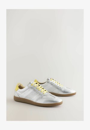 Ezüst bőr sportcipők sárga fűzőkkel és kiegészítőkkel, texturált panelek és bézs gumitalp. Könnyű és alacsony profilú dizájn.