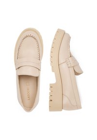 Béžové kožené mokasíny s robustnou, zúženou podrážkou a viditeľným šitím, ktoré majú charakteristický predný remienok a hladký povrch.