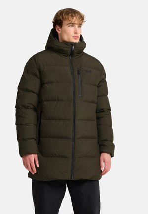 Mann trägt eine dunkelgrüne Steppjacke mit hohem Kragen und Frontreißverschluss, steht mit entspannten Händen an den Seiten und schaut leicht nach rechts.
