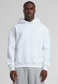 White hoodie made of soft fabric with a front pocket and a drawstring hood. Features ribbed cuffs and a relaxed fit.