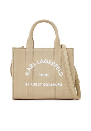 Bež torba iz tkanine z dvema ročajema, snemljivim ramenskim trakom in belim napisom "Karl Lagerfeld Paris 21 Rue St-Guillaume" na sprednji strani.